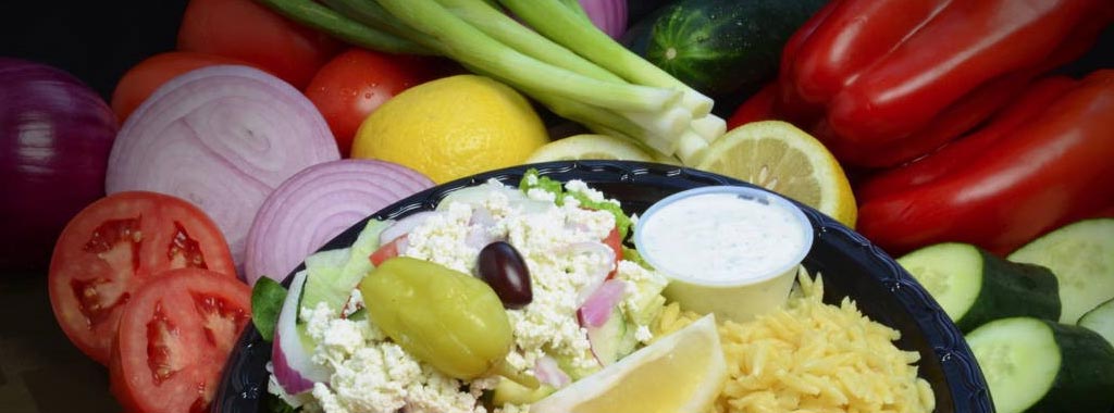 Fresh Mediterranean salad plate with vegetables, feta, lemon, and cucumber sauce